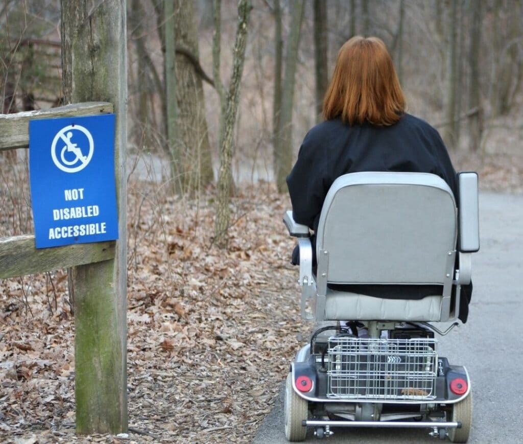 An individual in a wheelchair next to a sign that reads "NOT DISABLED ACCESSIBLE".